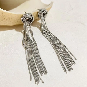Silver geometric chain tassel earrings with woven knot detail on beige ceramic display