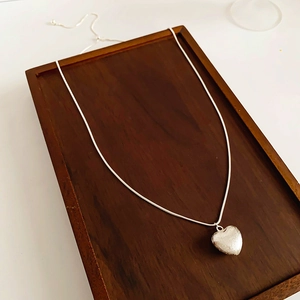Vue détaillée du pendentif cœur argenté brossé sur un plateau en bois foncé