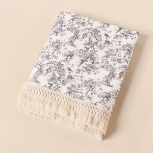 Close-up of Toile de Jouy print and cotton tassel trim on a soft muslin baby blanket