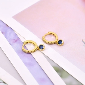 Close-up of gold hoop earrings with clear pave zircons and a deep blue round gemstone drop