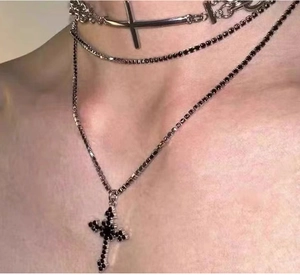 Close-up of layered silver metal necklaces with black gemstone and cross pendant details