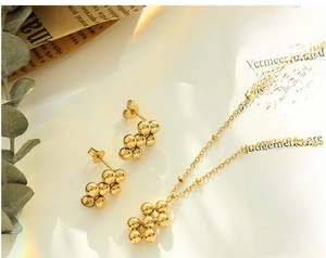 Detailed close-up of golden cluster bead necklace and earrings set with eucalyptus leaves