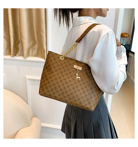 Brown printed tote bag with gold chain strap and a golden deer pendant on a model