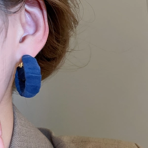 Close-up of royal blue velvet hoop earring with gold metal clasp worn by a model