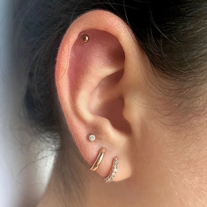 Close-up of gold stud earrings and zircon hoops worn on ear showing multi-piercing style