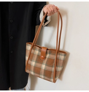 Detail of vintage brown plaid wool tote bag with leather straps on a black coat