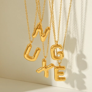 Chubby bubble initial pendant necklaces in gold plated stainless steel on beige background