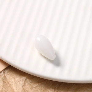 Macro shot of smooth white teardrop resin charm with jade texture on a textured plate