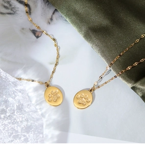 Detailed view of two gold cat paw pendant necklaces on silk fabric with crystal accents