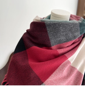 Detail of red and green plaid cashmere scarf featuring soft texture and tassel edges
