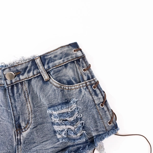 Detail der blauen Denim-Shorts mit seitlicher Schnürung, Metallösen und ausgefranstem Saum