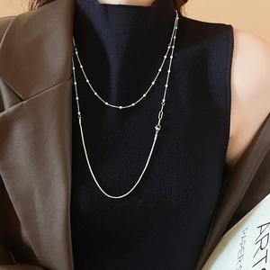 Detail of layered silver beaded and snake chain necklace on model over a black turtleneck