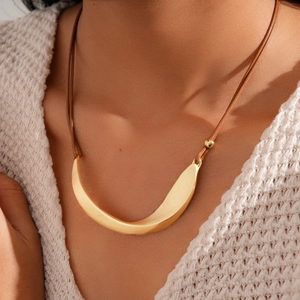 Detailed macro view of gold-tone irregular curved pendant on a brown cord necklace