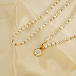 Elegant 18K gold plated pearl necklace with shell letter B pendant on beige silk fabric