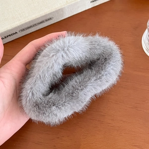 Détail d'une pince à cheveux grise en fausse fourrure tenue sur une table en bois