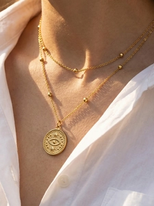 Détail d'un collier doré double rang avec perles et pendentif médaillon œil porte-bonheur