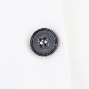 Detailed close-up of a black four-hole button on high-quality white twill midi dress fabric