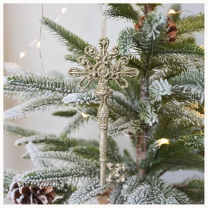 Macro shot of gold glitter vintage key ornament hanging on a snowy Christmas tree branch