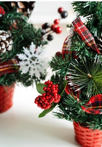 Detail of two mini tabletop Christmas trees with pine cones, berries, and plaid ribbons