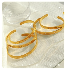 Detail of 18K gold plated zircon bracelets with starburst engravings on white backdrop
