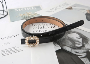 Detail of a black patent leather belt featuring a gold buckle with pearls and rhinestones