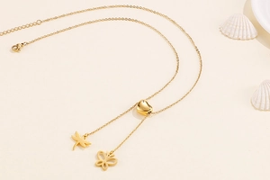 Détail macro d'un collier en Y doré avec fermoir coeur et pendentifs libellule et papillon
