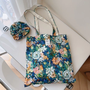 Close-up of floral oil painting cotton tote bag with matching scrunchie on a white table