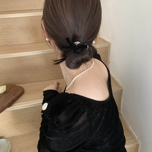 Elegant black velvet bow hair clip with silver accents on model with pearl necklace