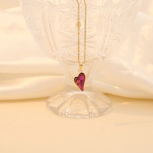 Elegant gold chain necklace with a deep red faceted glass heart pendant on a glass display