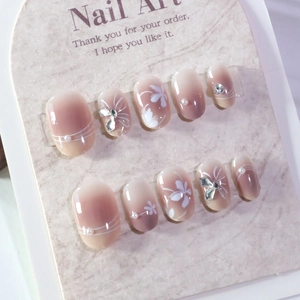 Short round press-on nails with blush gradient, white floral patterns, pearls, and crystals