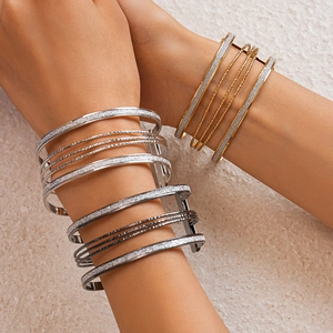 Detail of layered metal open bracelets with textured glitter finish and geometric design