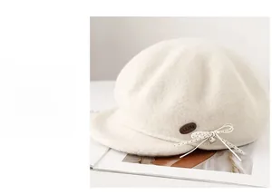 Detail of wool newsboy cap with cream bow, silver heart pendant and oval leather tag