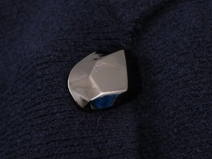 Macro shot of a faceted silver metal button on dark blue knit fabric detail