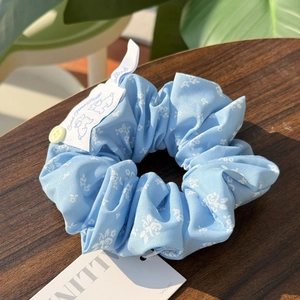 Macro view of light blue floral scrunchie with yellow button and cute pet woven label