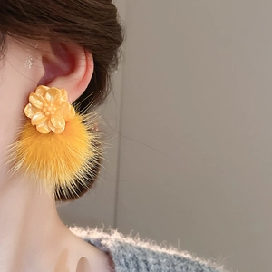 Close-up of yellow resin flower earrings with plush fur pompom on model for fashion detail