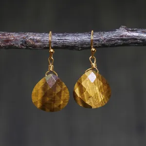 Detail of wire-wrapped tiger eye drop earrings hanging on a natural wooden branch