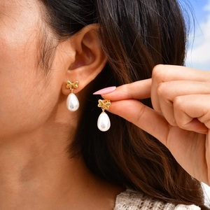 Close-up of elegant gold bow earrings with white teardrop pearls worn by a model