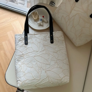 Detailed close-up of leaf embroidery texture and leather handle with gold rivets
