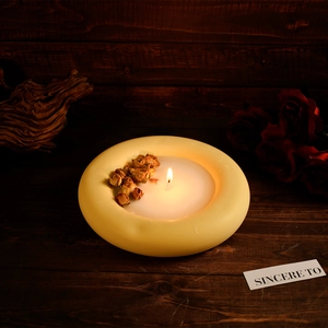 Close-up of a circular ring candle with dried flowers on a rustic dark wood surface
