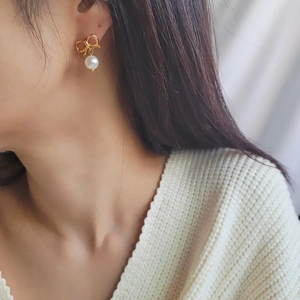 Gros plan de boucles d'oreilles nœud doré avec perles blanches portées à l'oreille