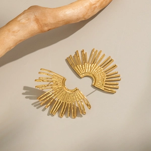 Detailed macro view of gold-plated striped fan earrings on a minimalist wooden display