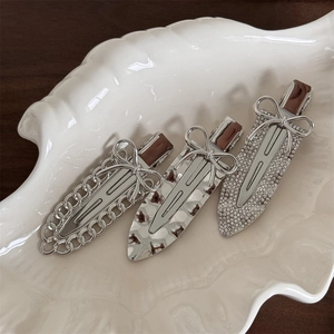 Three silver bow hair clips with chain, hammered, and rhinestone designs on white shell tray
