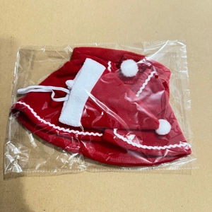 Flat lay of a red pet Christmas hat and cape set with white trim on a cardboard background