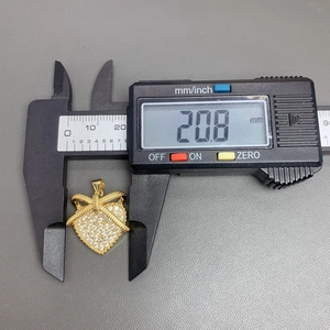 Macro view of a gold heart bow pendant showing 20.8 mm width on a digital caliper