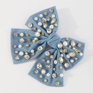 Dettaglio del fermaglio a fiocco in velluto blu con strass lucidi e perle bianche