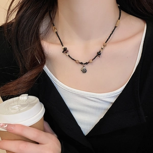 Detail of beaded necklace with black beads and a silver round pendant worn by a model