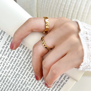 Detailed view of two gold rings with hollow leaf and heart designs on model hand