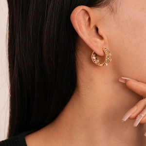 Détail de boucles d'oreilles créoles dorées avec perles et strass portées par un mannequin