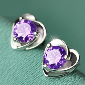 Macro shot of silver heart earrings featuring round cut purple gemstone on green fabric