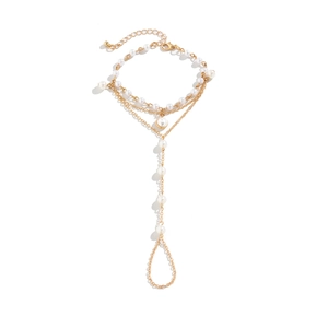 Detail of layered gold metal chain slave bracelet with white pearls and finger ring